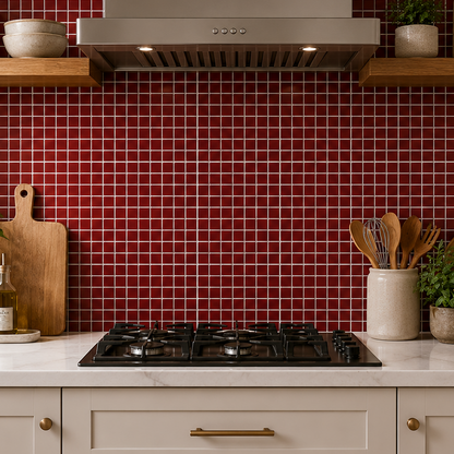 A modern kitchen scene with a red mosaic tile backsplash, white marble countertop, cream cabinets, a stainless steel range hood, and wooden floating shelves holding plants and decorative items.